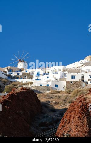 Eine weiß getünchte Windmühle und Hotels mit Balkonen auf der Spitze der vulkanischen Landschaft in Oia Santorini Stockfoto