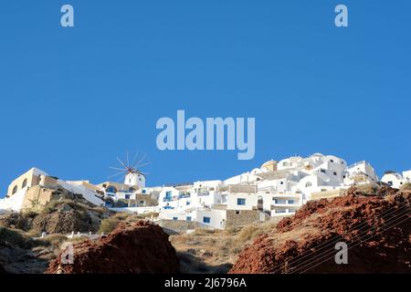 Eine weiß getünchte Windmühle und Hotels mit Balkonen auf der Spitze der vulkanischen Landschaft in Oia Santorini Stockfoto