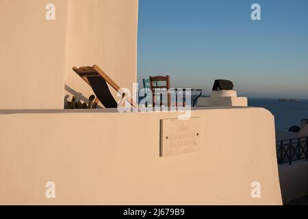 Oia, Griechenland - 11. Mai 2021 : Blick auf einen Balkon mit Stühlen und einem Tisch mit Blick auf die Ägäis mit einem Straßenschild „ PLOIARXON “ in Oia Santorini Stockfoto