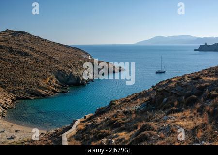 Blick auf den Strand von Valmas, ein Segelboot in der Ferne und einen Leuchtturm im Hintergrund auf der Insel iOS in Griechenland Stockfoto