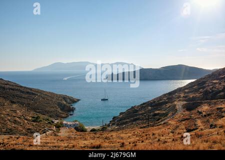 Blick auf den Strand von Valmas, ein Segelboot in der Ferne und einen Leuchtturm im Hintergrund auf der Insel iOS in Griechenland Stockfoto