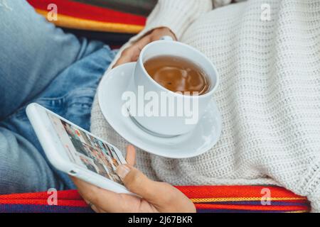 Junge Geschäftsfrau verwenden Smartphone für Social Media Marketing.Happy Millennial Check wie Follower Kommentar Entspannen Sie sich in der Hängematte Tee trinken.Adult Einfluss Stockfoto