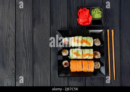 Köstliches Sushi auf einem schwarzen Teller, auf einem schwarzen Holzbrett liegen. Schwarzes Holzbrett mit Sushi-Set. Stockfoto