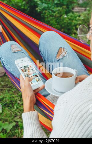 Junge Geschäftsfrau verwenden Smartphone für Social Media Marketing.Happy Millennial Check wie Follower Kommentar Entspannen Sie sich in der Hängematte Tee trinken.Adult Einfluss Stockfoto