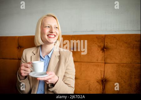 Porträt einer jungen schönen Frau, die in einem Café sitzt und Kaffee trinkt. Urlaub von der Arbeit. Pausenkonzept. Stockfoto
