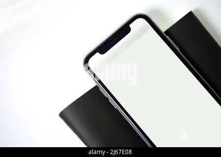 Smartphone mit schwarzem Leder-Notebook auf weißem Hintergrund. Stockfoto