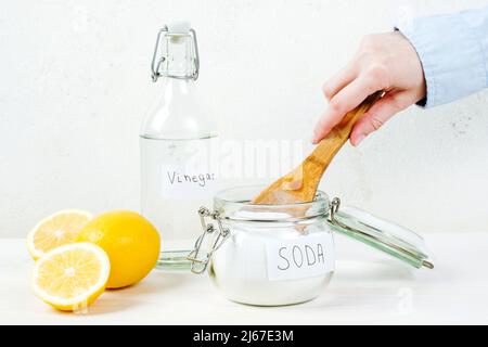 Weibliche Hand nimmt Backpulver in Glas Holzlöffel auf einem weißen Tisch. Das Konzept der organischen Fleckenentferner. Hochwertige Fotos Stockfoto