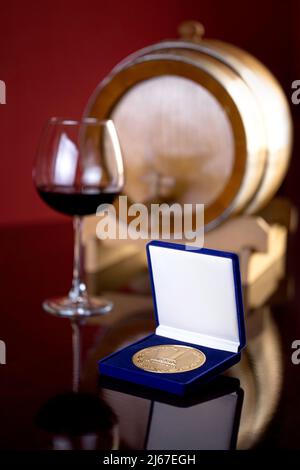 Siegermedaille in einer Geschenkbox auf dem Hintergrund eines Glases Wein. Stockfoto