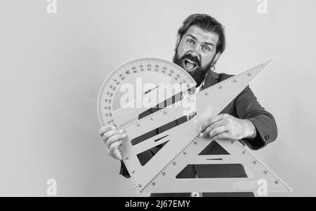 Bestehen Sie die Mathe-Prüfung. Lernen Sie das Thema. Glücklicher Mann mit Bart mit Dreieck und Winkelmesser. Studium der Messung. Formale Bildung. Männlicher Student Stockfoto