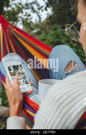 Junge Geschäftsfrau verwenden Smartphone für Social Media Marketing.Happy Millennial Check wie Follower Kommentar Entspannen Sie sich in der Hängematte Tee trinken.Adult Einfluss Stockfoto