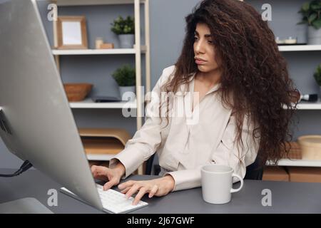 Nachdenklich konzentriert gebräunt liebenswert lockig lateinische Geschäftsfrau in Leinenhemd sitzen auf einem Stuhl im Heimbüro. Space Mockup Banner kopieren. Attraktiv Stockfoto