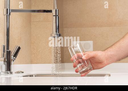 Ein leeres Glas in der Hand eines Mannes vor einem Wasserstrahl Stockfoto