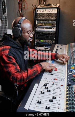 Vertikale Aufnahme eines modernen afroamerikanischen Tontechnikers, der mit einem Mischpult Musik kreiere Stockfoto