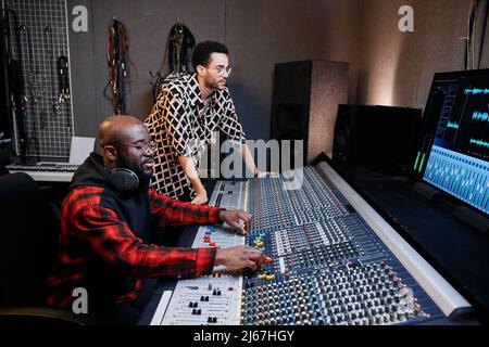 Reifer Black-Musikproduzent und junger männlicher Sänger arbeiten im Aufnahmestudio zusammen an Songs Stockfoto