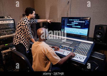 Professioneller afroamerikanischer Produzent und Musiker, der im Aufnahmestudio mit einem Mischpult Musiktitel erstellt Stockfoto