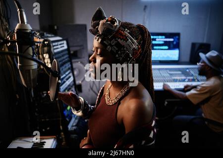 Schöne junge professionelle Sängerin in ethnischem Outfit, die singt, wenn sie das Lied im Studio aufnimmt Stockfoto