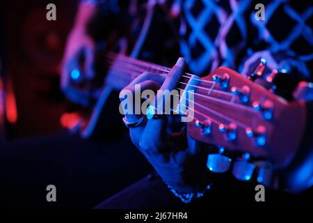 Mittlere Nahaufnahme eines nicht erkennbaren jungen Musikers, der in Neonlicht akustische Gitarre spielt Stockfoto