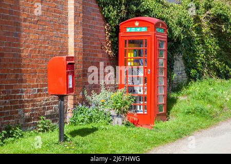 Rote englische Briefkasten und Telefonkiosks werden jetzt als Bücheraustausch genutzt und enthalten den Dorf-Defibrillator im Weiler Grafton Worcestershire Stockfoto