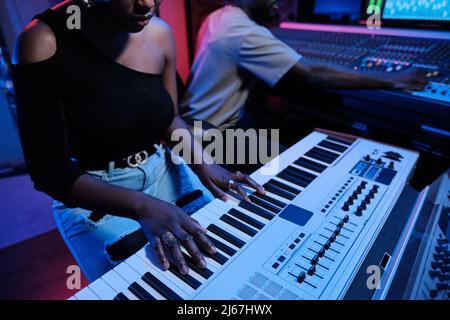 Afroamerikanische Frau spielt digitale Tastatur, während Musikproduzentin am Mixer im Aufnahmestudio, Neonbeleuchtung arbeitet Stockfoto