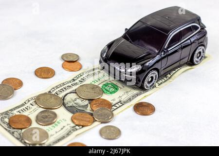 Schwarzes Spielzeug-Automobil mit usa-Dollar-Münzen auf hellem Hintergrund. Kfz-Versicherung, Auto-Service und Reparatur, Transport-Steuer-Konzept. Stockfoto