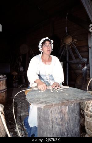 Williamsburg, VA. USA 9/1987. Korbweber. Master Korb Weber mit Holzstreifen in einem Korb von vielen Größen gewebt zu tragen oder zu speichern Gemüse, Maisähren, Obst, Eier, Nähgeräte, Feuerholz für die Küche, Feuerholz für den Herd und Waschlappen. Die Korbweberei ist 1000s Jahre alt. Stockfoto