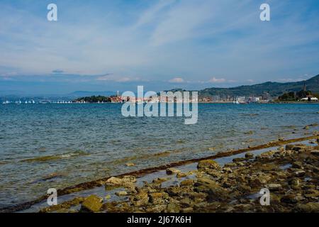 Ein felsiger Strand an der Adriaküste Sloweniens in der Nähe von Izola. Die Stadt Izola ist im Hintergrund Stockfoto