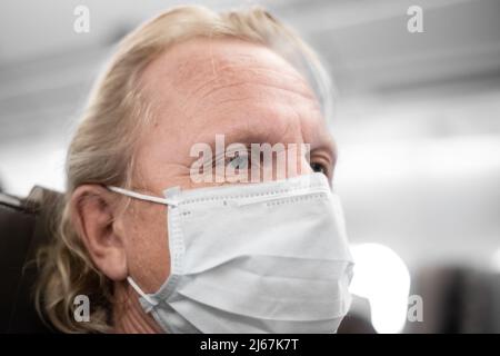 Reifer Mann in einer medizinischen Maske, mit müden, schmerzenden Augen in der Kabine. Flugreisebeschränkungen, Coronavirus-Prävention. Stockfoto