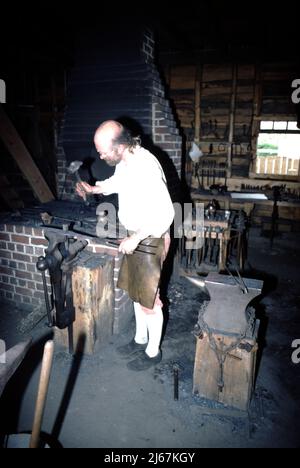 Williamsburg, VA. USA 9/1987. Meisterschmiede für Colonial Williamsburg. Diese Schmiede basteln die Metallbefestigungen, die von anderen Handwerkern aus Colonial Williamsburg verwendet werden, wie zum Beispiel den Radrecher, die Hausbefestigungen wie Nägel, Scharniere und Verriegelungen, und cooper-Eimer- und Laufbänder sowie landwirtschaftliche Ausrüstung und Reparatur. Stockfoto