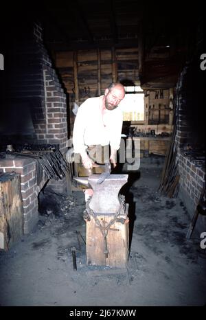 Williamsburg, VA. USA 9/1987. Meisterschmiede für Colonial Williamsburg. Diese Schmiede basteln die Metallbefestigungen, die von anderen Handwerkern aus Colonial Williamsburg verwendet werden, wie zum Beispiel den Radrecher, die Hausbefestigungen wie Nägel, Scharniere und Verriegelungen, und cooper-Eimer- und Laufbänder sowie landwirtschaftliche Ausrüstung und Reparatur. Stockfoto