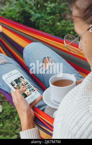 Junge Geschäftsfrau verwenden Smartphone für Social Media Marketing.Happy Millennial Check wie Follower Kommentar Entspannen Sie sich in der Hängematte Tee trinken.Adult Einfluss Stockfoto