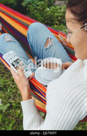 Junge Geschäftsfrau verwenden Smartphone für Social Media Marketing.Happy Millennial Check wie Follower Kommentar Entspannen Sie sich in der Hängematte Tee trinken.Adult Einfluss Stockfoto