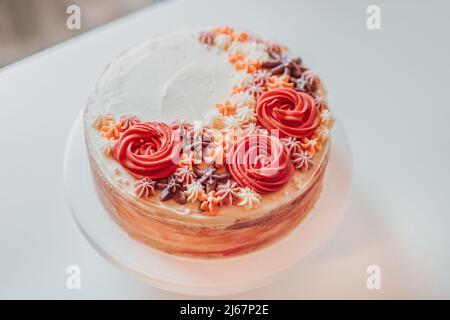 Hausgemachter klassischer Vanillemarmor-Sahnetorte, bestreut mit cremigen Blumendekorationen auf einem weißen Teller, Retro-Rustikale Farbdekoration und Ornamenten Stockfoto