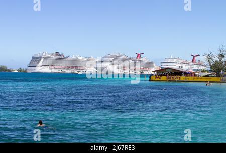 Touristen schwimmen und spielen im wunderschönen türkisfarbenen Wasser des Nassau Harbour, den Bahamas, mit Kreuzfahrtschiffen im Hintergrund. Stockfoto