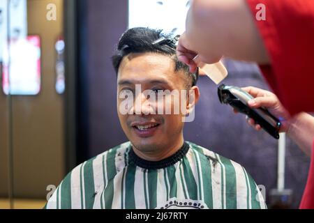 Porträt eines lächelnden asiatischen Mannes, der auf einem Friseurladen sitzt Stockfoto
