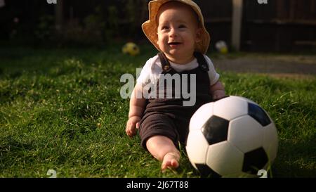 Happy Baby Sitzt Mit Fußball Schwarz Weiß Classic Ball Auf Grünem Gras. Entzückendes Kleinkind Baby Spielt Im Garten Im Garten Im Freien. Kleine Kinder Mit Stockfoto