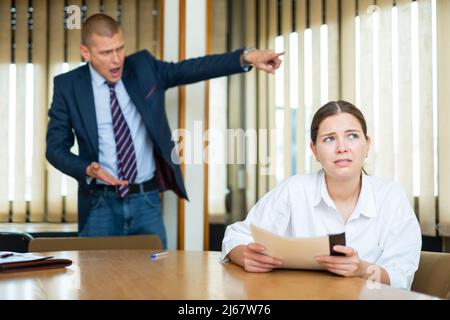 Emotionaler junger Chef beschimpft seine Sekretärin im Konferenzraum Stockfoto