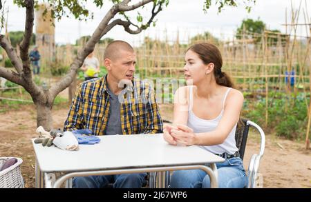 Mann und Frau kommunizieren, sitzen am Tisch in ihrem Garten Stockfoto
