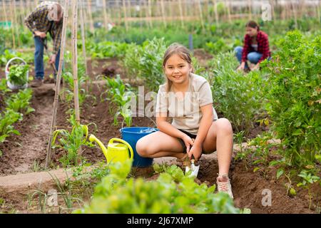 Positive Mädchen mit Chopper entfernt Unkraut aus Gartenbeeten Stockfoto