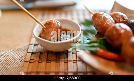 Nahaufnahme, thailändische Isaan-Wurst, die in spezielle traditionelle Sauce getaucht wird. Gegrillter fermentierter Reis und Schweinefleisch. Stockfoto