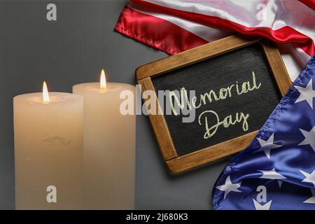 Tafel mit Text MEMORIAL DAY, USA-Flagge und brennenden Kerzen auf dunklem Hintergrund Stockfoto