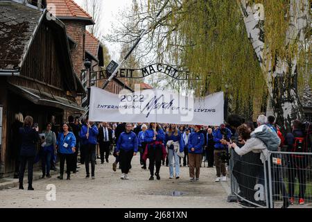 Auschwitz, Polen. 28. April 2022. Die Teilnehmer des Marsches der Lebenden halten ein Transparent mit der Aufschrift Internationaler Marsch der Lebenden und Durchschreiten des Tores Arbeit Macht frei. Am Internationalen Holocaust-Gedenktag nehmen Teilnehmer aus verschiedenen Teilen der Welt am Marsch der Lebenden Teil. Der Marsch der Lebenden ist eine Hommage und ein Zeichen des Gedächtnisses für die Holocaust-Opfer. Die Teilnehmer des Marsches fahren gemeinsam über die drei Kilometer lange Strecke vom Tor Arbeit Macht frei im ehemaligen deutschen Lager Auschwitz I zum ehemaligen Standort Auschwitz II - Birkenau. Kredit: SOP Stockfoto