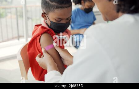 Der afroamerikanische Arzt trägt nach der Impfung Gips auf die Schulter eines Kindes auf. Öffnen Sie die Ärmel, um bei der Heilung gegen Grippe oder Epidemie zu impfen Stockfoto