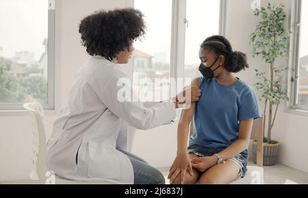 Der afroamerikanische Arzt trägt nach der Impfung Gips auf die Schulter eines Kindes auf. Öffnen Sie die Ärmel, um bei der Heilung gegen Grippe oder Epidemie zu impfen Stockfoto