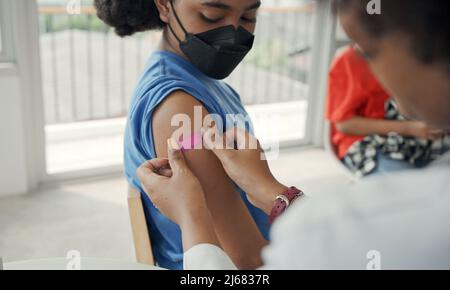 Der afroamerikanische Arzt trägt nach der Impfung Gips auf die Schulter eines Kindes auf. Öffnen Sie die Ärmel, um bei der Heilung gegen Grippe oder Epidemie zu impfen Stockfoto