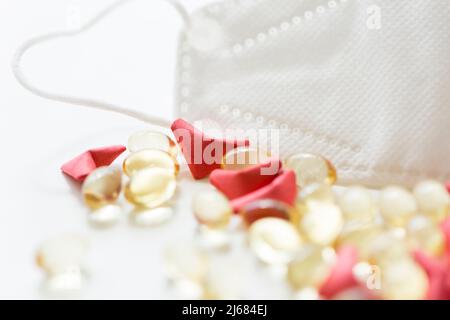 Rotes herzförmiges Origami, weiche Kapsel Softgel und N95 Gesichtsmaske auf weißem Hintergrund - Stock Foto Stockfoto