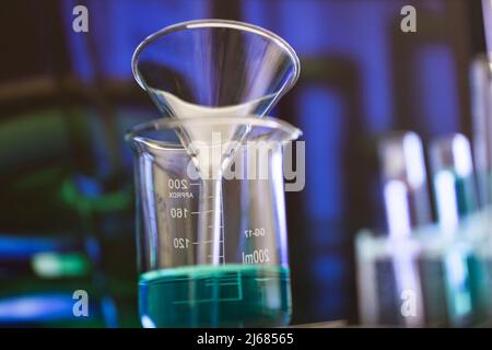 Trichter aus kristallklarem Glas in einem Becher, gefüllt mit blauem chemischem Reagenz - Stock photo Stockfoto