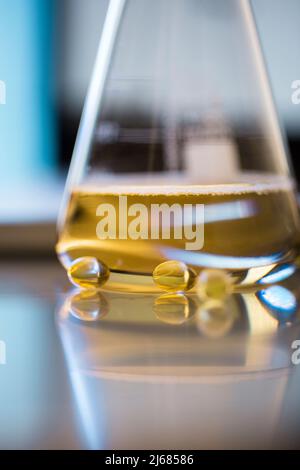 Konische Flasche mit goldener Flüssigkeit, Medizin mit weichen Kapseln und Trichter - Stock Foto Stockfoto