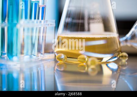 Konische Flasche mit goldener Flüssigkeit, Medizin mit weichen Kapseln und Trichter - Stock Foto Stockfoto