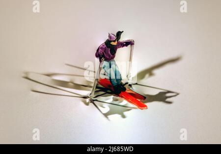 Miniaturfigur eines Mannes, der auf farbenprächtigen roten Skiern auf Winterschnee fährt, umgeben von mehreren Schatten und Copyspace Stockfoto