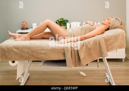 Seitenansicht einer ruhigen barfuß-Frau, bedeckt mit einem Handtuch, das auf dem Tisch liegt und die Therapie im modernen Schönheitssalon genießt Stockfoto